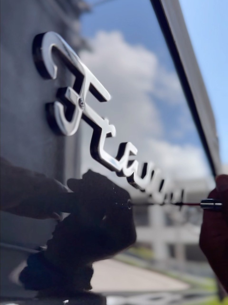 Mirror finish on a dark yacht hull polished by Correct Reflect, sky and clouds reflected in the paint